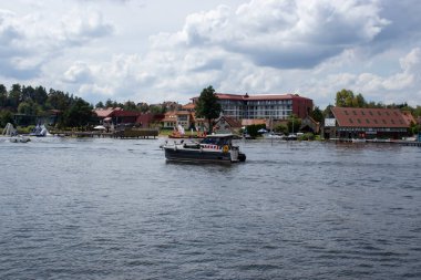 Mikolajki Polonya - 20 Eylül 2024: Mikolajki 'nin dingin atmosferini yansıtan büyüleyici binalar ve yemyeşil göllerle çevrili bir teknenin manzarası.