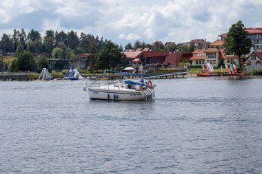 Mikolajki Polonya - 20 Eylül 2024: Pahalı manzaralar ve büyüleyici deniz manzaralarıyla çevrili gölde süzülen bir yelkenlinin sakin manzarası.