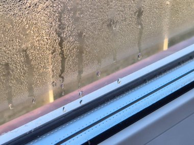 Penceredeki su damlacıklarının yakın görüntüsü, yumuşak ışık arka planına sahip yoğunlaşma efektlerini gösteriyor. Hava değişikliklerini ya da ev atmosferlerini tasvir etmek için mükemmel..