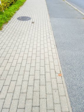 Şehir fotoğrafçılığı için ideal çimen ve asfalt yollarla çevrili taş kaldırımlı ve rögar kapaklı bir kaldırım manzarası..