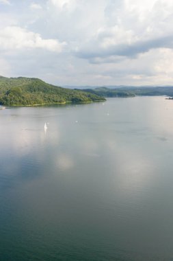 Bulutlu gökyüzünün altında yemyeşil tepelerle çevrili sakin bir göl manzarası dinlenmek için mükemmel huzurlu bir atmosfer yaratıyor..