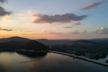 Sakin bir gölün üzerinde sakin bir günbatımı gökyüzünün canlı renklerini yansıtıyor. Yeşillik suları sarar ve huzurlu bir atmosfer yaratır..