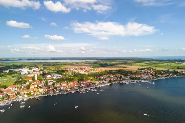 Mikolajki Polonya 'nın göl kenarındaki renkli evlerde ve parlak mavi gökyüzünün altında yemyeşil renkli teknelerle manzaraları gösteren hava manzarası.