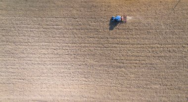 Parlak güneş ışığı altında faaliyet gösteren tarımsal makineleri gösteren bir traktörün hava görüntüsü.