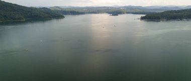 Orman tepeleriyle çevrili sakin bir göl manzarası doğanın ve açık hava güzelliğinin özünü yakalıyor..