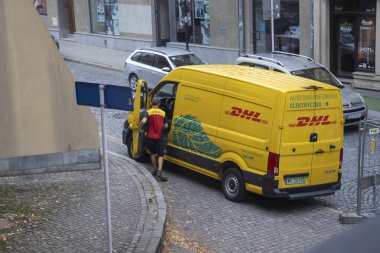 Rzeszow Poland - October 3 2023: A DHL delivery van is parked on a cobblestone street as a courier prepares to unload packages. Urban logistics in action. clipart