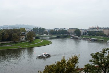 Cracow, Polonya - 20 Eylül 2022: Krakow 'daki Vistula Nehri' nin rıhtım boyunca kayıklar ve yemyeşil alanlarla manzaralı manzarası, kentin huzurlu cazibesini yansıtıyor.