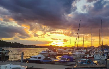 Mikolajki Polonya - 20 Eylül 2024: Gökyüzü turuncu ve mor renkli canlı renklerle boyanırken marina teknelerinin üzerinde huzurlu bir gün batımı.