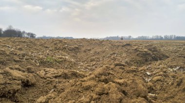 Kırsal bir alanda yeni sürülmüş toprağın yakın çekimi bulutlu bir gökyüzünün altında toprak dokularını ve tonlarını gözler önüne seriyor..