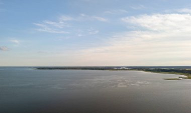 Berrak mavi gökyüzünün altında yemyeşil bir göl ile çevrili sakin bir hava manzarası, rahatlama ve doğa meraklıları için mükemmel..