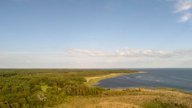 Berrak mavi gökyüzünün altında yemyeşil ormanlarla birleşen manzaralı bir nehrin çarpıcı hava manzarası. Doğa severler ve sükunet arayanlar için mükemmel..