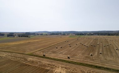 Temiz bir gökyüzünün altında saman balyalarının yuvarlandığı geniş bir tarla manzarası kırsal alanların güzelliğini gözler önüne seriyor..