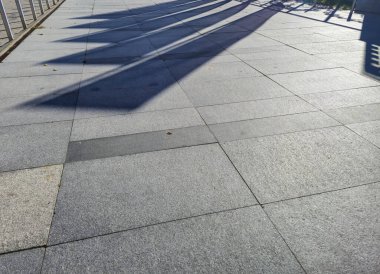 Güneş ışığıyla aydınlanan kaldırım gölgelerin soyut bir desen oluşturduğunu gösteriyor. Arkaplan ya da mimari projeler için ideal.