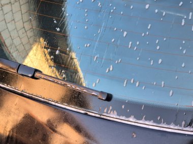 Yıkanırken ön camı ıslak bir arabanın arkasında. Binanın yansıması sabun baloncuklarında görülebilir. Otomotiv ve temizlik temaları için mükemmel.