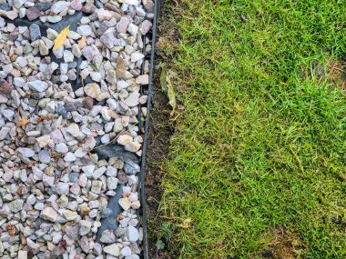 A close-up view of pebbles on one side and freshly mowed grass on the other illustrating a beautiful transition between hardscape and landscape. Perfect for landscaping themes. clipart