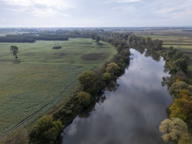 Bereketli yeşillik ve tarım alanlarında kıvrılan sakin bir nehrin manzarası doğanın dingin güzelliğini yakalıyor..