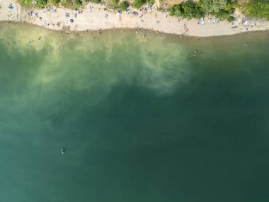 Güneşlenenlerin sıcak yaz gününün tadını çıkardığı sakin bir sahil manzarası.