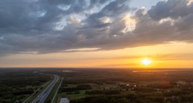 Gün batımında bir otoyolun çarpıcı hava manzarası gökyüzünde canlı renkler ve aşağıdaki yemyeşil manzaralar sergiliyor..