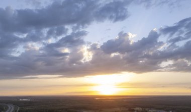 Geniş bir arazide gün batımı bulutları aydınlatıyor ve gökyüzündeki sıcak renkler sakin bir atmosfer yaratıyor..