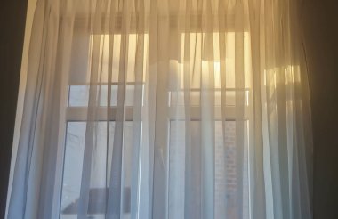 Yumuşak güneş ışığı katıksız perdelerin arasından süzülüyor ve bir odada sıcak bir davetkar atmosfer yaratıyor.
