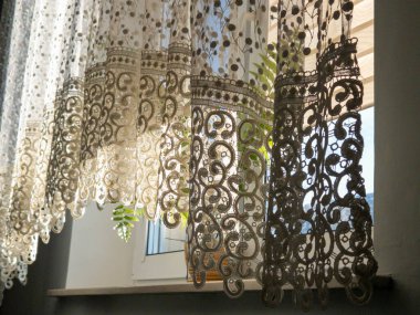 Zarif dantel perdeler güneşli bir pencerenin üzerine nazikçe örterek güzel bir ışık ve gölge oyunu yaratıyor..