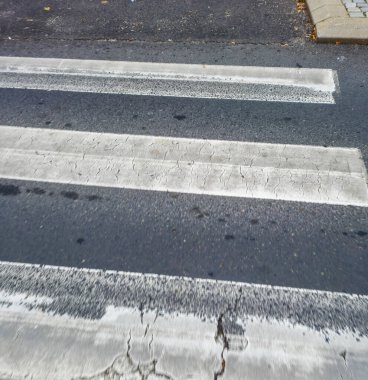 Şehir altyapısını ve yaya yollarını aydınlatan gri asfalt bir yolda açık beyaz çizgili yaya geçidinin yakın görüntüsü.