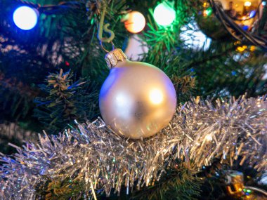 Neşeli ışıklar ve süslemelerle çevrili bir ağaca asılı gümüş bir Noel süsü. Parlak ve neşeli bir tatil süsü..