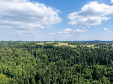 Parlak bir gökyüzü altında yemyeşil ormanların ve rüzgar türbinlerinin havadan görünüşü