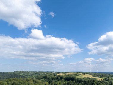 Yeşil tepeleri ve mavi gökyüzünün altında rüzgar türbinleri olan ve çevresel temalar için mükemmel kabarık bulutları olan güzel bir manzara.