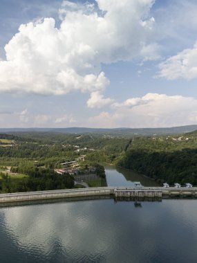 Polonya 'daki Solina barajının manzarası yemyeşil ve bulutlu bir gökyüzünün altında yansıtıcı bir göl sergiliyor..
