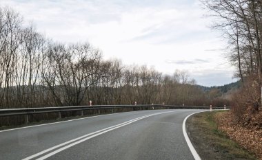 Etrafı çıplak ağaçlarla çevrili dolambaçlı bir yol, sabahın erken saatlerinde sakin bir manzarayı gözler önüne seren ufka götürür..
