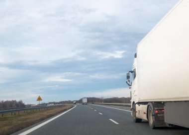 Etrafı doğa ile çevrili bulutlu bir gökyüzünün altındaki bir otoyolda beyaz bir kamyon. Açık yol, özgürlük ve seyahat anlamına gelir..