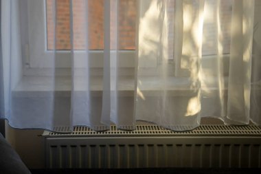 Yumuşak güneş ışığı perdelerin arasından süzülüyor ve pencerenin kenarına nazikçe yansıyor.