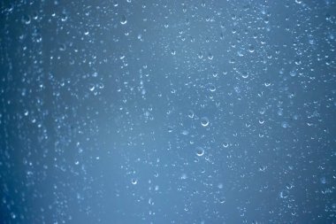 Cam yüzeydeki yağmur damlalarının yakın çekimi bulanık mavi bir zemin oluşturur. Sakin ya da melankolik olmak için mükemmel bir yol..