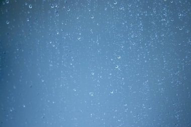 Mavi arkaplandaki yağmur damlalarına yakın çekim sakinleştirici bir atmosfer yaratır. Doğa ve hava durumu için mükemmel.