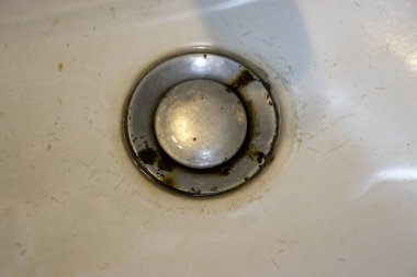 Kirli lavabonun yakın plan görüntüsü. Görünür pas ve saç kalıntıları günlük bakım sorunlarını vurguluyor..