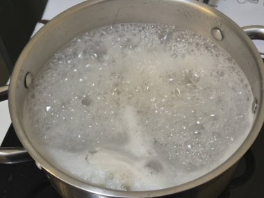 Paslanmaz çelik bir tencerede kaynayan suyun yakın çekimi yemek pişirme ve mutfak aktivitelerini temsil eden kabarcıklar ve buhar yaratır..