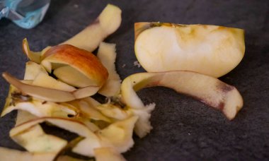 Taze elma dilimleri ve atık kabukları sağlıklı beslenme ve yemek hazırlama temalarını vurgulayan karanlık bir yüzeye yerleştirildi. Mutfak ve yaşam tarzı içeriği için ideal.