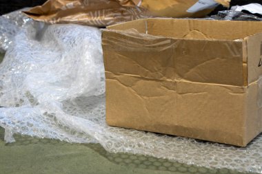 Karton bir kutu ve baloncuk ambalajı, ambalaj ve nakliyeyi sembolize eden desenli bir yüzey üzerinde. E-ticaret ve lojistik temalar için ideal.