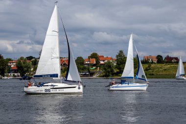 Mikolajki Polonya - 29 Eylül 2024: İki yelkenli sakin bir göl boyunca zarif bir şekilde süzülüyor ve manzaralı bir manzarada eğlence amaçlı yelken açıyor.