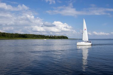 Mikolajki Polonya - 29 Eylül 2024: Sakin sularda süzülen bir yelkenlinin sakin manzarası, bereketli yeşillik kaplıyor kıyıda, açık havada huzurlu bir günün özünü yakalıyor..