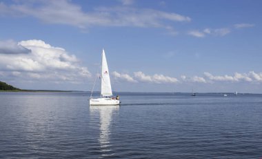 Mikolajki Polonya - 29 Eylül 2024: Pofuduk bulutlar altında sakin sularda süzülen bir yelkenlinin sakin manzarası.