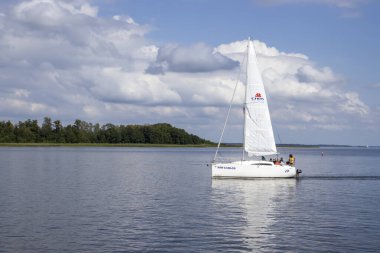 Mikolajki Polonya - 29 Eylül 2024: Bereketli yeşillik ve mavi gökyüzü ile çevrili sakin sularda süzülen sakin bir yelkenli