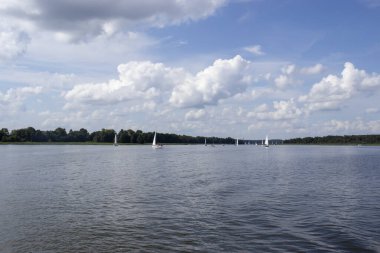 Mikolajki Polonya - 29 Eylül 2024: Yelkenli tekneler ve gökyüzünde kabarık bulutlar ile gölün manzarası doğanın huzur veren güzelliğini yansıtıyor.