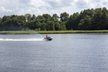 Mikolajki Polonya - 29 Eylül 2024: Serin bir göl üzerinde jet ski süren bir kişi yemyeşil ve canlandırıcı su sporları faaliyetleri sergiliyor.