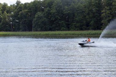 Mikolajki Polonya - 29 Eylül 2024: Yeşilliklerle çevrili bir gölde jet ski ile heyecan verici bir yolculuk yapan bir kişi. Macera ve eğlence temaları için mükemmel..