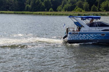 Mikolajki Polonya - 29 Eylül 2024: Bereketli yeşilliklerle çevrili sakin sularda gezen renkli bir tekne boş zaman aktiviteleri için mükemmel.