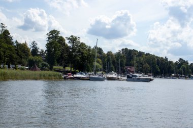 Mikolajki Polonya - 29 Eylül 2024: Mikolajki botlarındaki marina manzarası yemyeşil ve güzel bulutlu gökyüzü doğa severler için mükemmel.