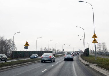 Rzeszow Polonya - 3 Temmuz 2024: Hareket halindeki araçlar uyarı ve gri gökyüzü ile şehir yolu sahnesi. Ulaşım ve altyapı temaları için ideal.