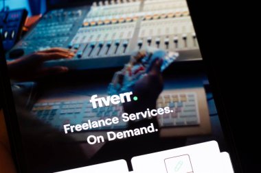 Varşova Polonya - 10 Mart 2025: Fiverr uygulamasını ses ekipmanlarıyla modern bir çalışma ortamında sergileyen akıllı telefon.